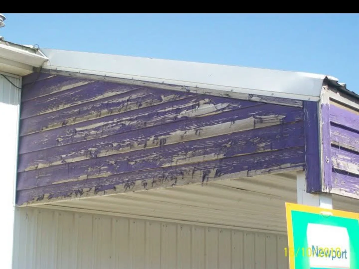Before: close view of faded purple wood boards and weathered trim at the corner of the store facade