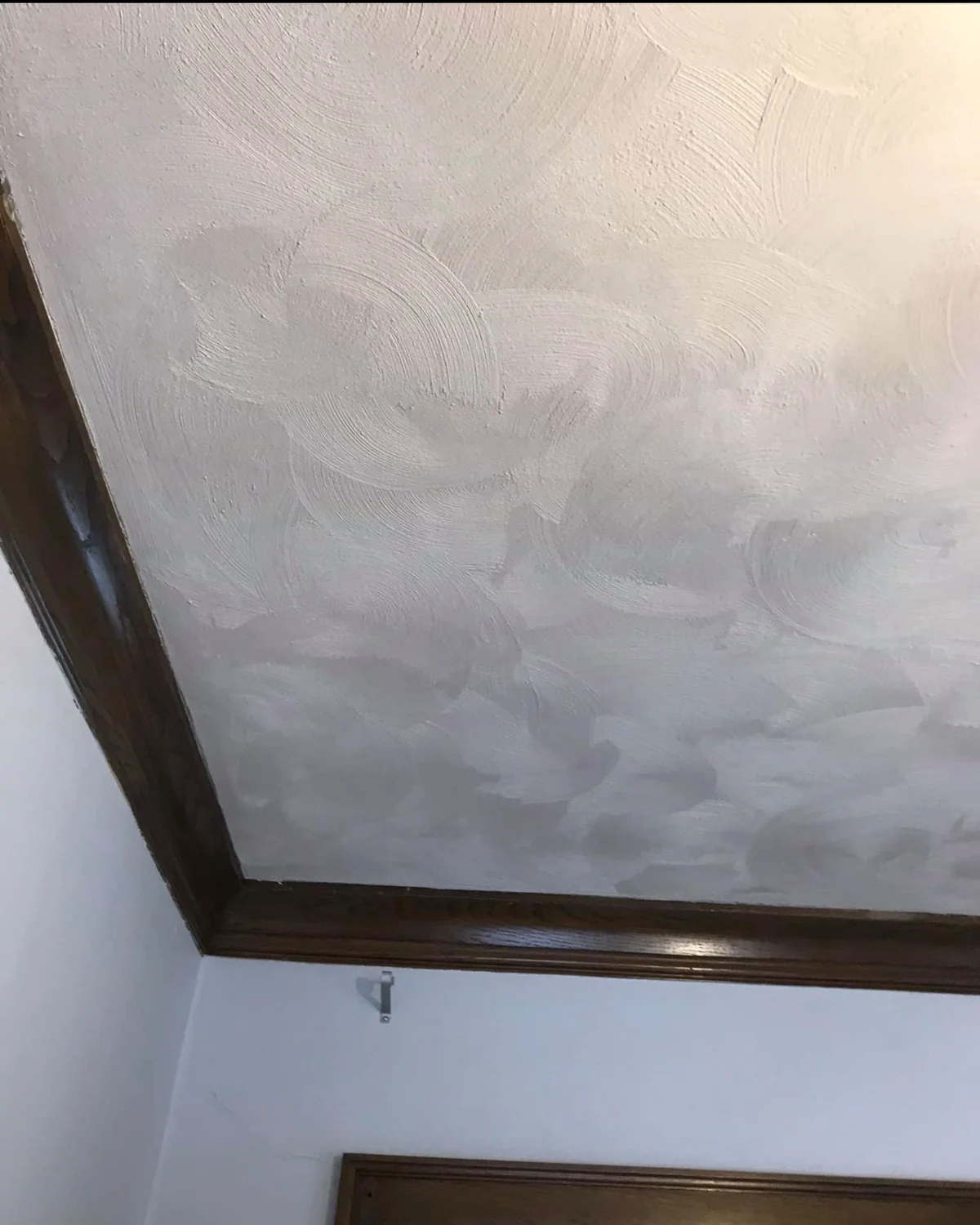 Detail of the pale calico plaster texture beside dark wood trim at the ceiling edge