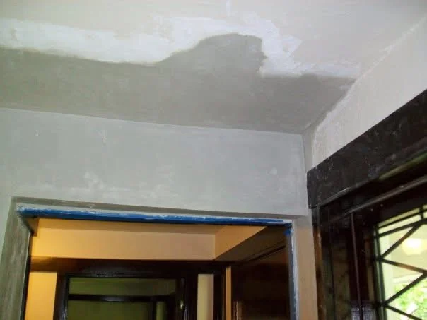 During: gray base-coat plaster filling the water-damaged area above a doorway, edges taped