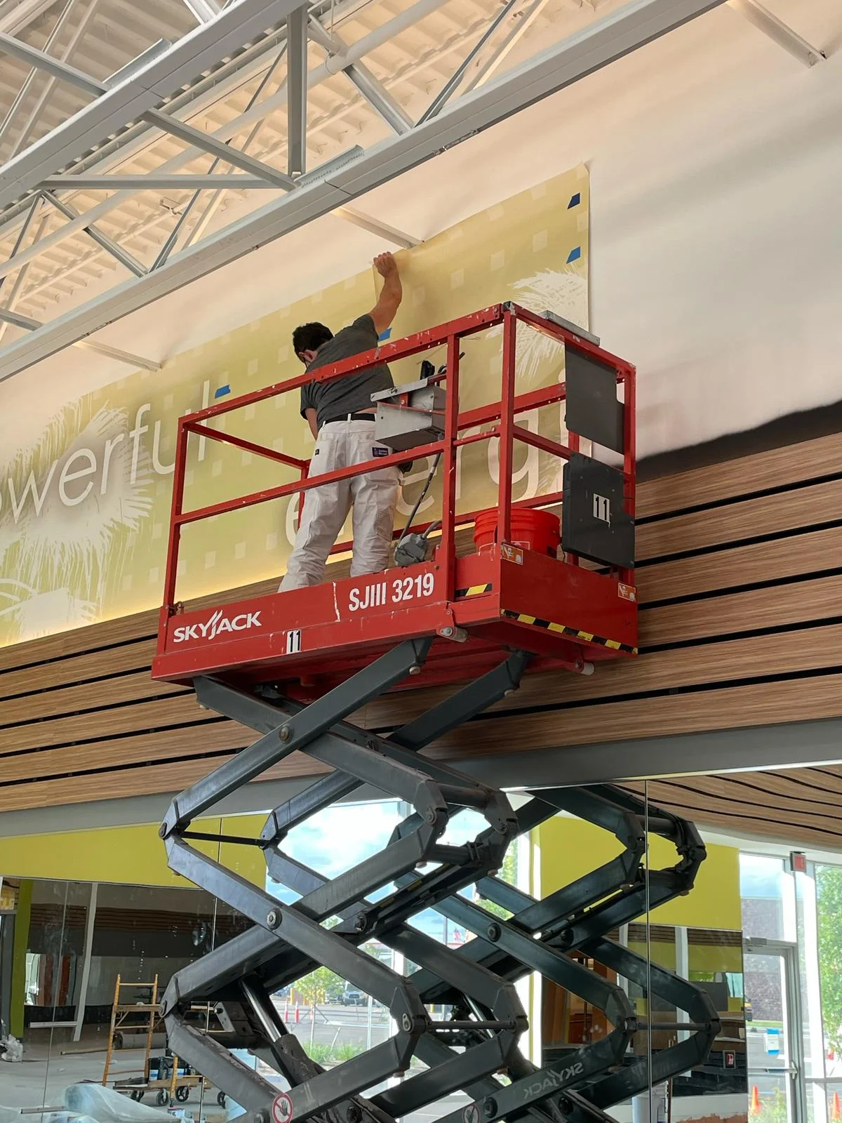 Installing a large printed wall covering high on a gym wall from a red scissor lift