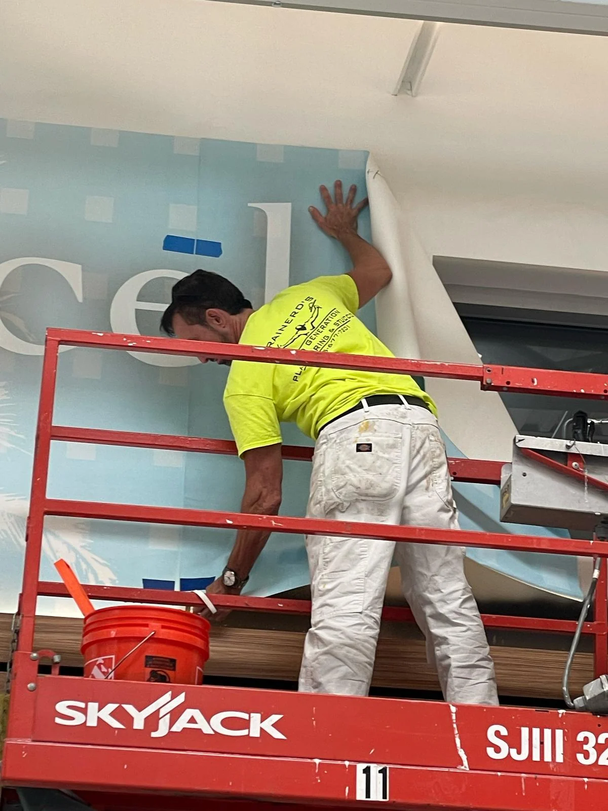 Smoothing a large printed wall-covering panel by hand from the scissor lift