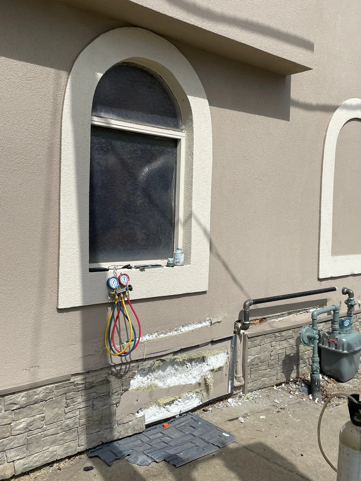 Before: EIFS torn open below an arched window after a vehicle impact, with white insulation foam and mesh exposed and a base panel knocked off the wall