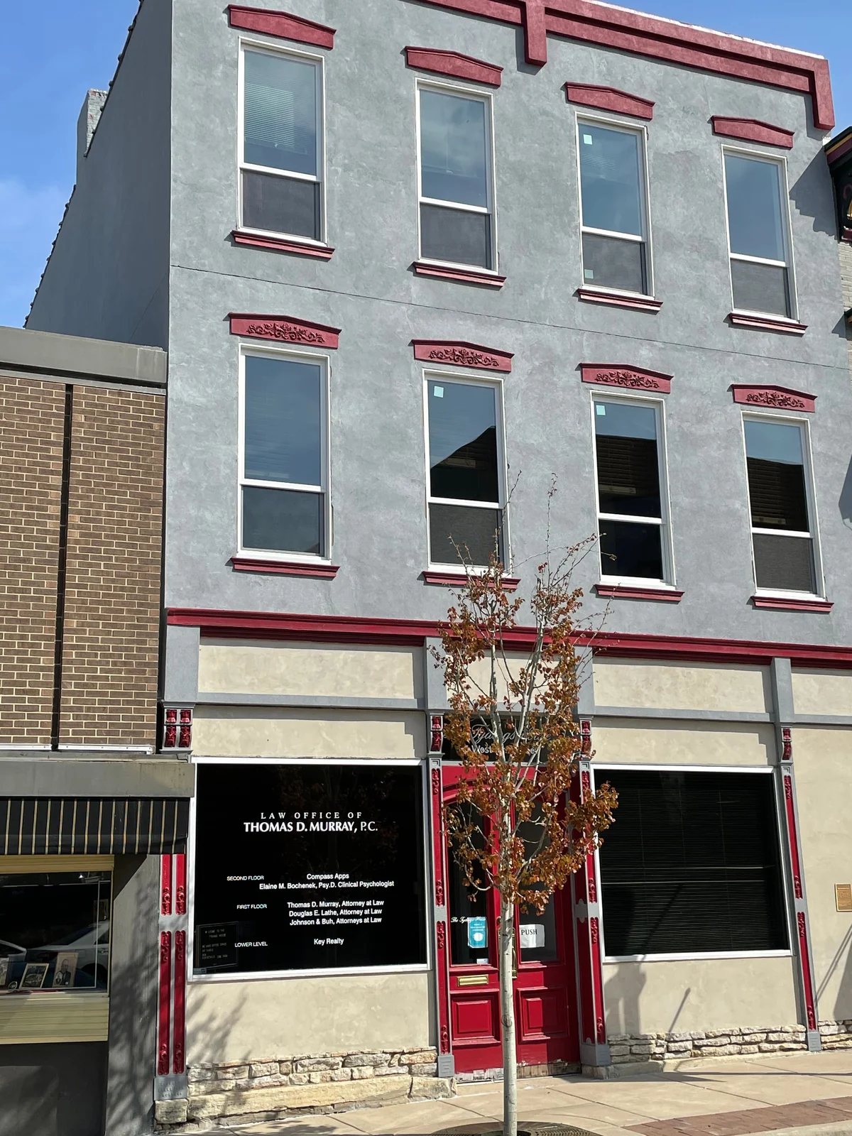 The finished three-story storefront: gray stucco facade with red cornice, window hoods and storefront trim
