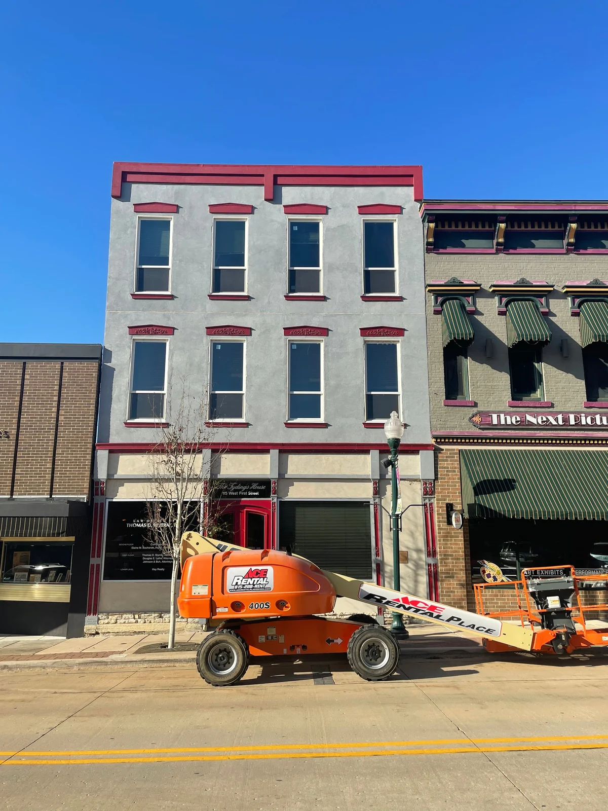 The storefront on the job, with an orange boom lift parked at the curb beneath the stucco facade
